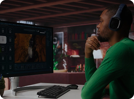Een man in een groene trui en met een koptelefoon op kijkt aandachtig naar een video op een computerscherm in een gezellige, goed verlichte kamer met boekenkasten op de achtergrond